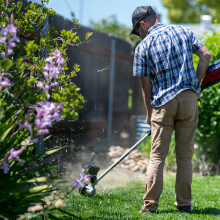 picture of a man weedeating next to a fence and flowers